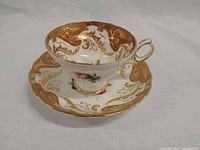 Tea cup and saucer set shown from an angle to display interior gold gilt decoration and floral hand-painted pink rose details
