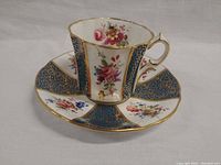Tea cup and saucer set shown from front angle highlighting floral and blue gilt panel design with gold trim.