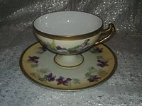 Tea cup on matching saucer showing floral design and gold paint.