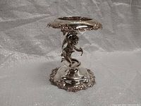 Front angle view showing cherub figure, floral edges on base and top, reflective silver plating