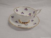 Photo of tea cup and saucer showing purple sweet violet floral pattern and gold trim on scalloped edges.