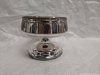Front and side view of the silver-plated dish or chalice showing reflective surface and detailed engraved Roman figures on the outer bowl band.