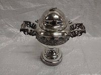 Front view of the vintage silver-plated sugar bowl with lid on, showing detailed floral embossed spoon holder handles and pedestal base.