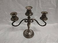 Front angle view of vintage silver-plated three-arm candelabra showing ornate detailing and overall condition.