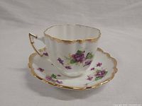 Tea cup and matching saucer plate showing floral design and gold rim on white background.