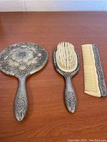 Full view of the three-piece vintage dressing table set on a wood surface showing hand mirror, hairbrush, and comb.