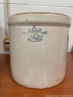 Side view of the antique crock showing blue crown emblem with number 2 on beige glazed ceramic.