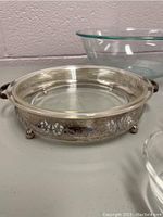 Silver-plated serving dish showing detailed floral engraving and rounded feet on white surface.