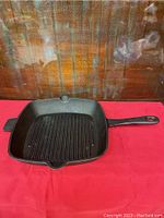 Front view of the square cast iron grill skillet showing the long handle, helper handle, pour spouts, and ridged cooking surface.