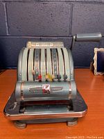 Front view of vintage metal check writer with five dials and right side lever on a chrome base.