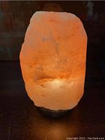 Himalayan pink salt lamp glowing with warm orange light on wooden base.