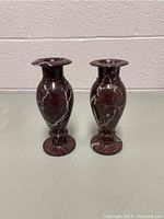 Pair of deep reddish-brown marble vases with white veining on a flat surface against a white brick wall background.