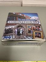 Overhead view of the Coronation Street DVD Trivia Game in a metal tin box, showing detailed cover art featuring TV show characters and logo.