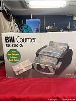 Photo of the original product box showing the Royal Sovereign RBC-1200-CA bill counter, detailing speed (1,100 bills per minute) and capacity (130 bills).