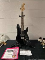 Full front view of Spectrum black electric guitar on stand with amplifier and accessories laid out.