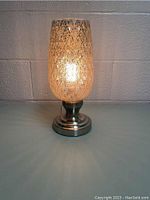Full view of the table lamp showing the crackled glass shade illuminated and metal base.