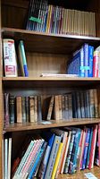 Full bookshelf with multiple shelves showing antique books. Top shelf has lined up slim volumes and beige bound books. Middle shelf has worn hardcover books with faded and torn dust jackets and cloth bindings. Bottom shelf has modern educational and paperback style books.