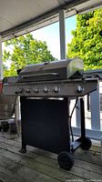 Full view of TeraGear gas BBQ grill showing six knobs, curved lid, wheels, and sturdy frame.