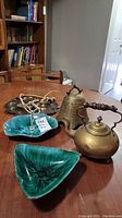 Two green glazed BMP serving dishes, brass teapot and large brass bell on a table