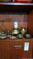 Shelf with six brass candle holders including a handle style and scalloped base, two small round brass dishes, and two brass urns.