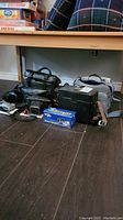Multiple camera bags, cases, and boxes grouped on floor under table.