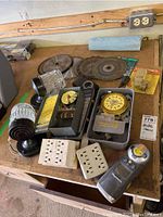 Assortment including saw blades, timer boxes, outdoor lights, and outlet plates on a wooden table.