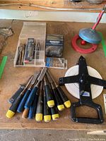 Full arrangement showing chisels laid out on a wood surface, a plastic tape measure, and a plastic organizer box with drill bits and screws inside.