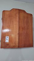Closed wooden dart board cabinet showing natural wood grain finish and curved top edges.