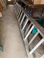 Side view of the full length of the aluminum extension ladder showing the tubular rails and rungs.