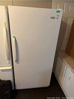 Front view of white Woods upright freezer with handle and brand label visible