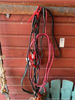 Three used jumper cables hanging, red and black clamps visible, cables coiled and tangled.