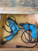 Two Makita corded drills in a wooden drawer: one hammer drill and one electric drill, showing general wear and wiring intact.