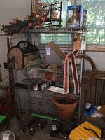 Full view of the vintage metal shelf showing wire shelves with various items on them and attached wooden handle.
