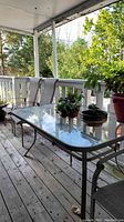 Full view of the rectangular glass top patio table with metal frame and several metal mesh chairs around it on the wooden porch.