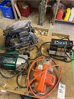 Overview of four power tools displayed on wooden bench, showing belt sander, planer, grinder sharpener, and jigsaw with cables.