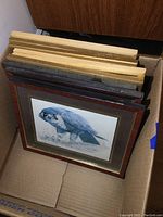 Box containing nine stacked framed prints, visible are different frame styles including dark wood and light wood