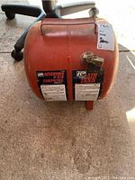 Front view of the orange portable air tank showing valve and part of label.
