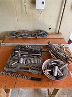 Wide shot of the socket set case with assorted sockets and ratchets, bowl of additional sockets, multiple wrenches, and five metal pulleys.