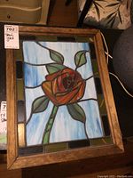 Full view of stained glass panel showing rose, leaves, and border in wood frame