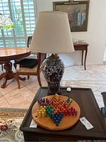 Photo showing the ceramic Asian styled lamp with floral patterns and beige fabric shade alongside the wooden Chinese Checkers board with multicolored pegs arranged for play.