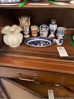 Shelf display of various blown glass and ceramic miniature items including vases, cups, platter, and decorative shoes.