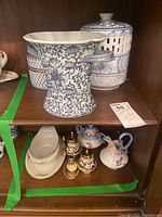 Photo showing full set on wooden shelf with various ceramic items, including vase, candle burner, salt and pepper shakers, and tableware.