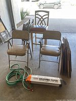 Five chairs visible: four beige folding chairs and one wooden framed high chair; garden hose coiled and U-Haul wrapping paper box in front