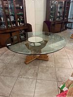 Full view of round glass top dining table showing clear glass and carved wooden base on tiled floor.