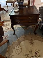 Front angled view of wooden end table with two drawers and brass handles, showing cabriole legs and top surface with minor wear.