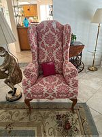 Front view of fireside wingback chair showing red and beige damask fabric and small red pillow.