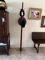 Full view of the tall wooden hat rack standing against a white wall near furniture and artwork.