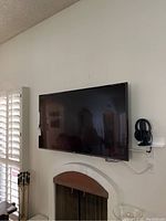 Front view of LG 55-inch TV mounted on wall above fireplace with headphones on a shelf nearby.