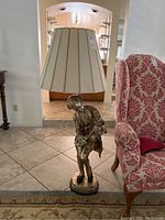 Full view of Mozart figure floor lamp with beige lampshade and detailed base on tiled floor next to pink patterned chair.