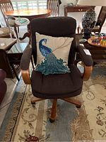 Front view of brown cushioned office chair with wooden armrests and base, featuring decorative peacock-themed throw pillow